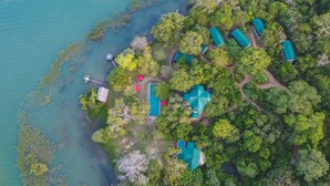 An aerial view of a resort with several green-roofed cabins surrounded by dense greenery and a body of water. - Flameback Eco Lodge (Weerawila)