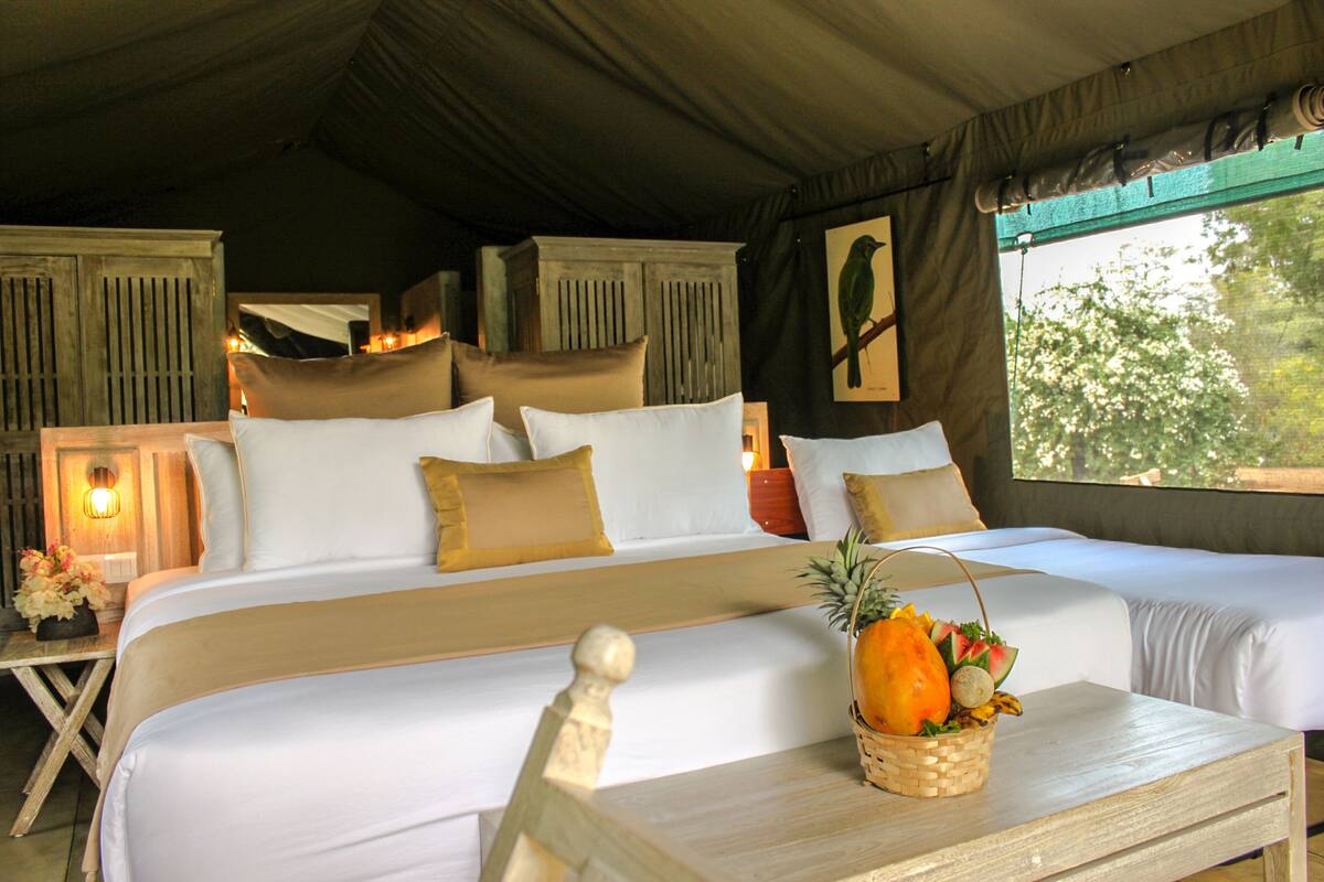 A large bed with multiple pillows, a wooden headboard, and a nightstand with a basket of fruit.