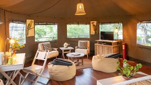 A tented accommodation with a wooden floor, a bed, seating area with bean bags, a small table, and a television. - Flameback Eco Lodge (Weerawila)