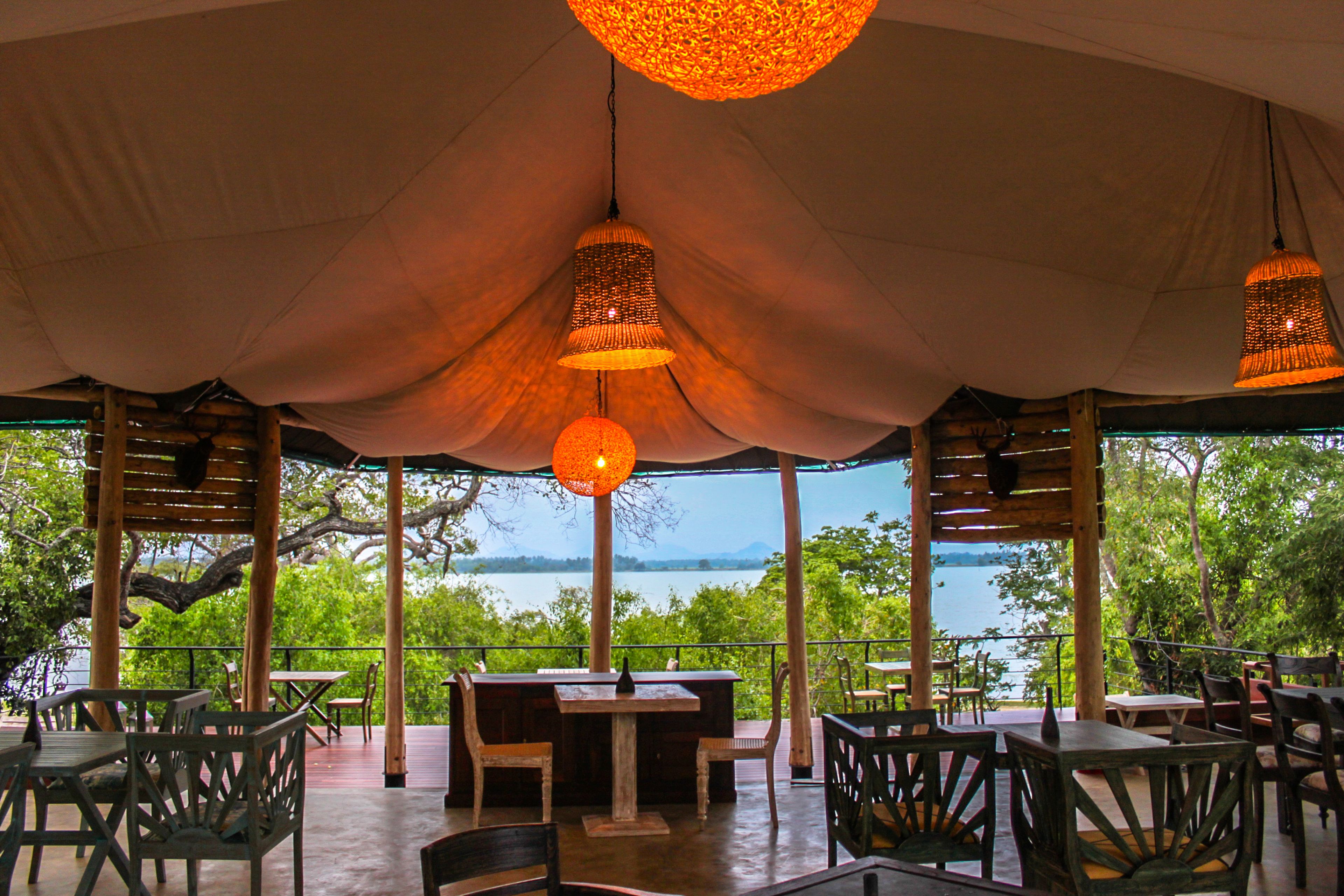 Un área de comedor al aire libre con mesas y sillas, un paraguas grande y vistas a un lago.