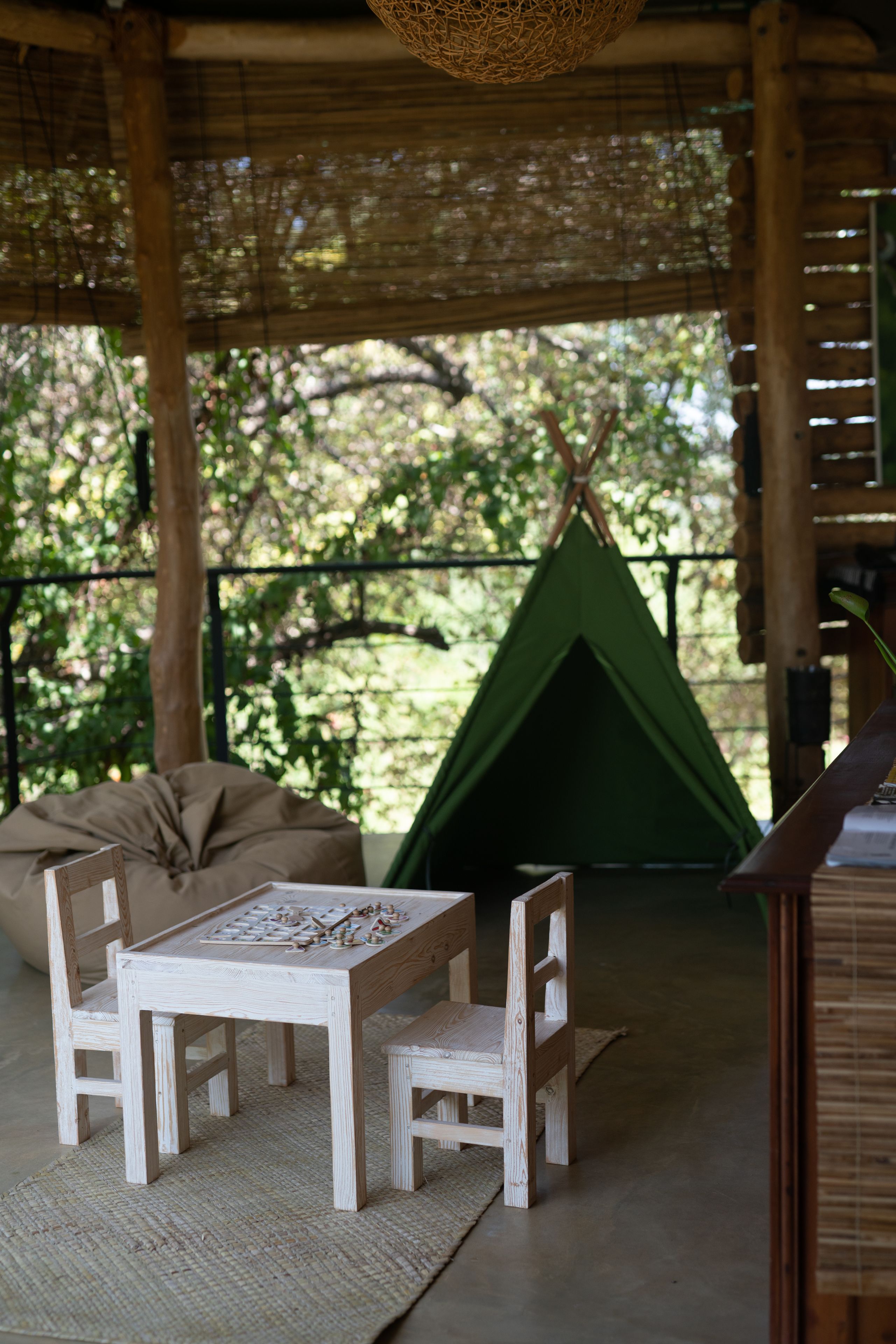 A wooden table with chairs, a green teepee, and a woven ceiling in a rustic setting.