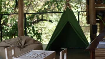 A wooden table with chairs, a green teepee, and a woven ceiling in a rustic setting.