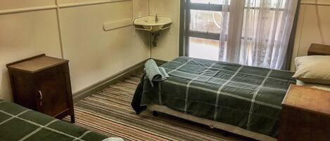 A hotel room with two beds, a small sink, a mirror, and a window with curtains.