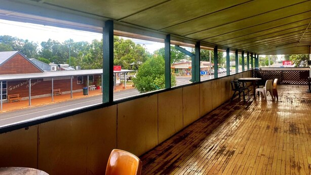 Un espace extérieur abrité, doté d’un plancher en bois et offrant une vue sur une rue bordée d’immeubles et d’arbres.