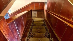 Un escalier en bois avec une moquette à motifs, un panneau d’avertissement et une main courante.
