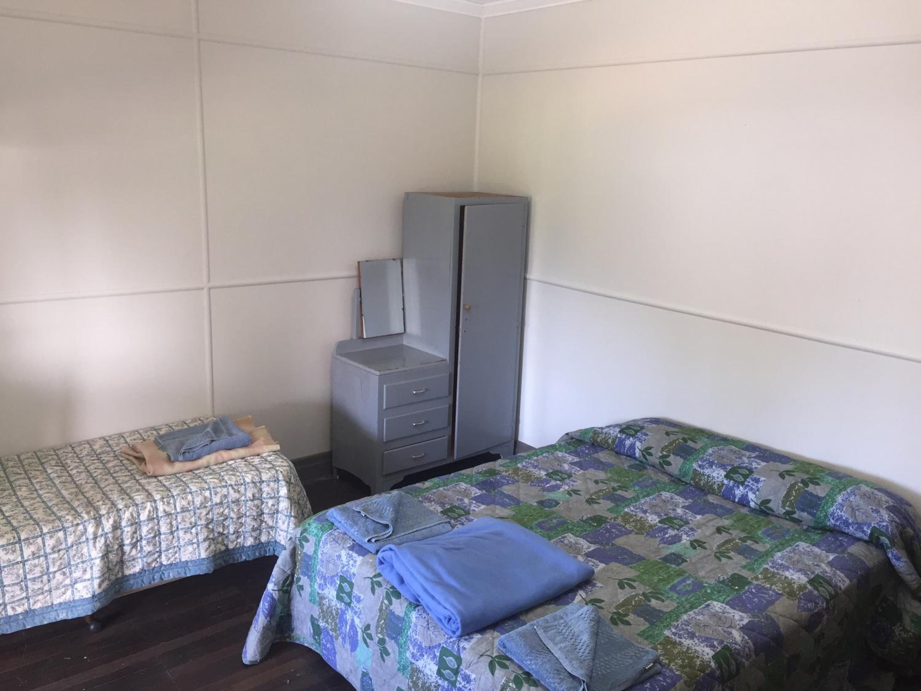 A room with two beds, a wardrobe, and a small table.