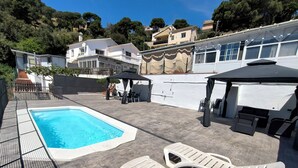 A swimming pool with lounge chairs, a covered seating area, and a view of surrounding buildings.