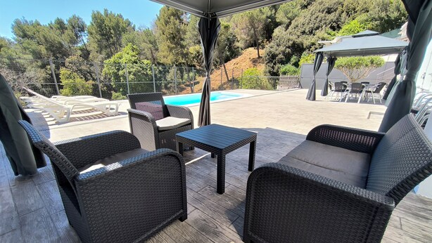 An outdoor patio with wicker furniture, a pool, and a view of trees and hills.