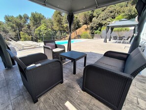 An outdoor patio with wicker furniture, a pool, and a view of trees and hills.