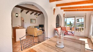Un salon chaleureux avec une table en bois, un canapé et un téléviseur. Des arches donnent accès à une autre pièce et à un balcon offrant une vue agréable.