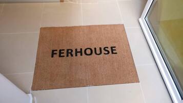 Tapete marrom com a palavra "FERHOUSE" sobre um chão de azulejos.