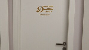Une porte blanche fermée, ornée d’un logo et d’une inscription indiquant « FERHOUSE Dreams MARINHEIROS », ainsi que d’une poignée de porte.