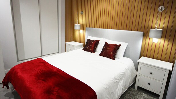 Une chambre d’hôtel avec un grand lit, deux tables de chevet, un plaid rouge et des panneaux de bois aux murs.