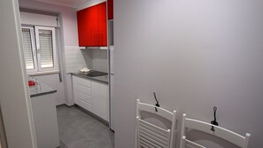 A compact kitchen with white cabinets, a red upper cabinet, a built-in stove, and a small countertop.