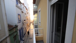Une rue étroite, bordée de bâtiments des deux côtés, une personne qui marche et un balcon avec une balustrade.