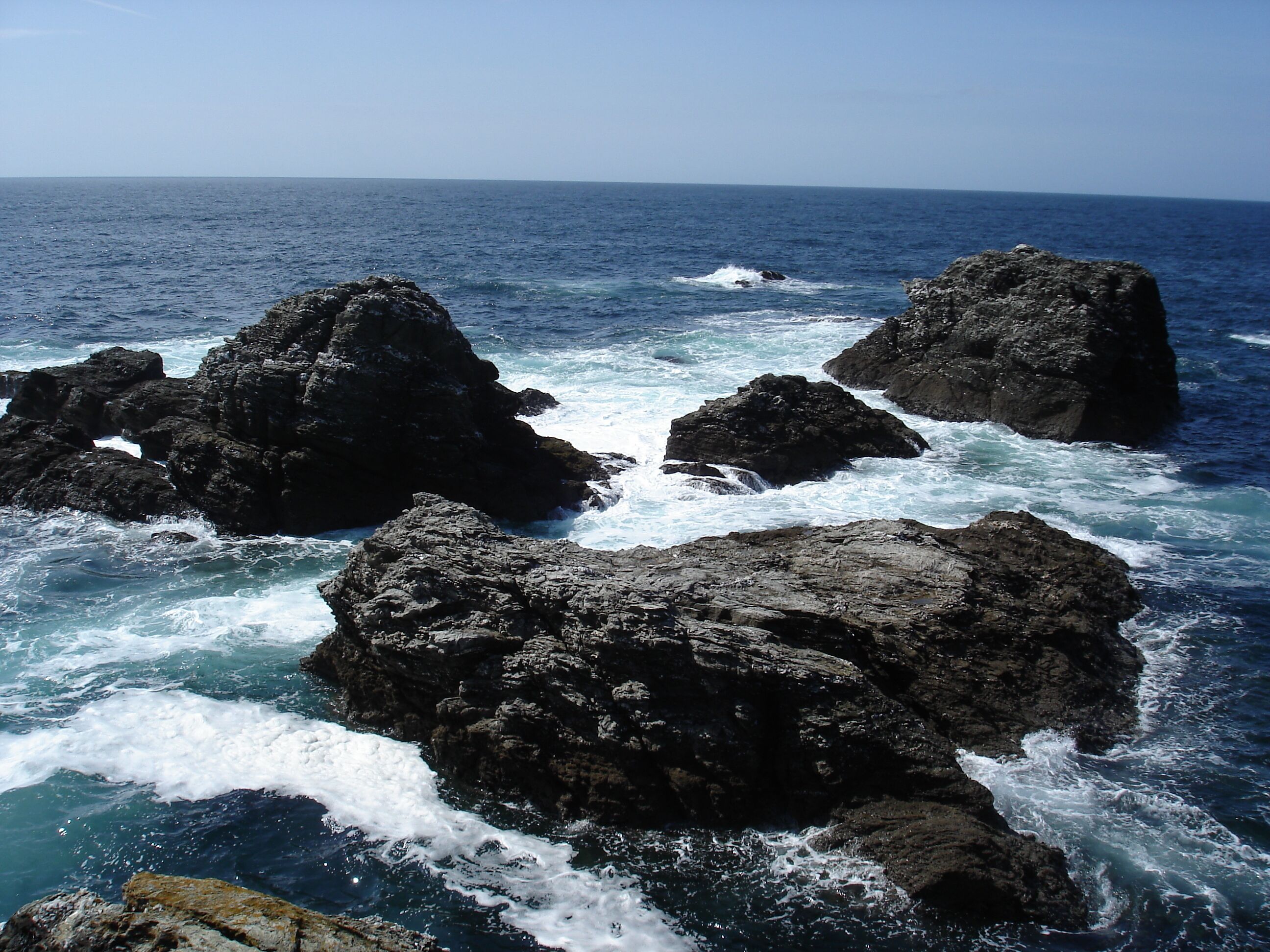 A coastal scene with large dark rocks and the ocean.