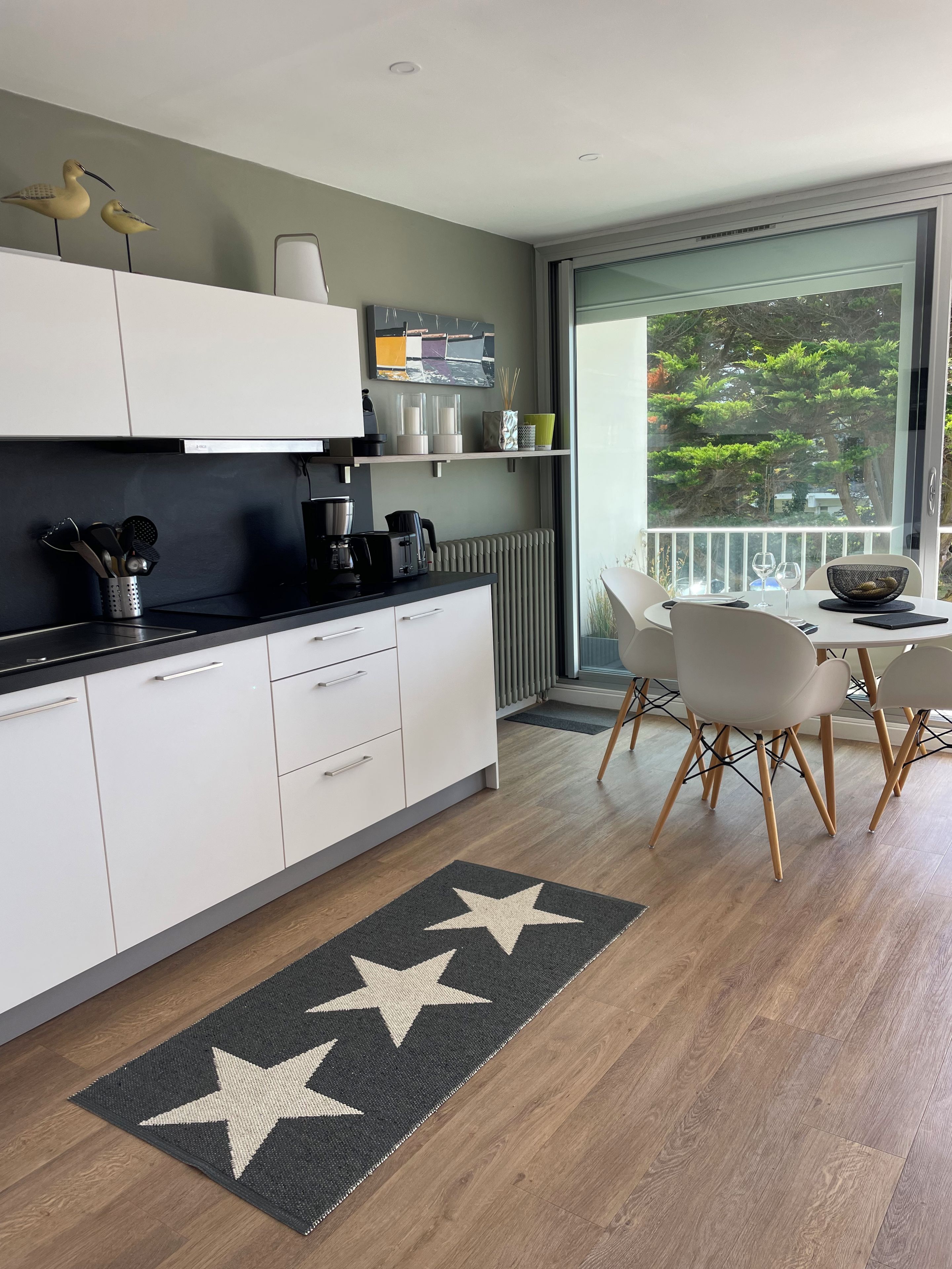 A modern kitchen with white cabinets, a black countertop, and a dining area with a table and chairs.