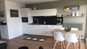 A modern kitchen with white cabinets, a black countertop, and a dining area with a wooden table and white chairs. - Nice sea view, south facing, Wifi, Parking, 50 m from beach & Thalasso (Quiberon)