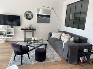 A modern living room with a grey sofa, black chairs, a glass coffee table, a white rug, a TV, and a large window. - Nice sea view, south facing, Wifi, Parking, 50 m from beach & Thalasso (Quiberon)