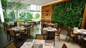 A restaurant with multiple tables set for dining, a large green wall, and a view of greenery outside. - Vinos Asia at Swiss Garden (Kuala Lumpur)