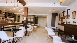 A modern cafe with white chairs, wooden tables, and hanging pendant lights.
