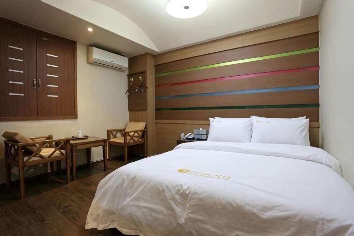 A hotel room with a bed, a desk, and a chair. There is an air conditioning unit on the wall.