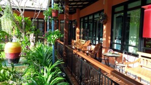 An outdoor seating area with wooden tables and chairs, surrounded by greenery and potted plants.