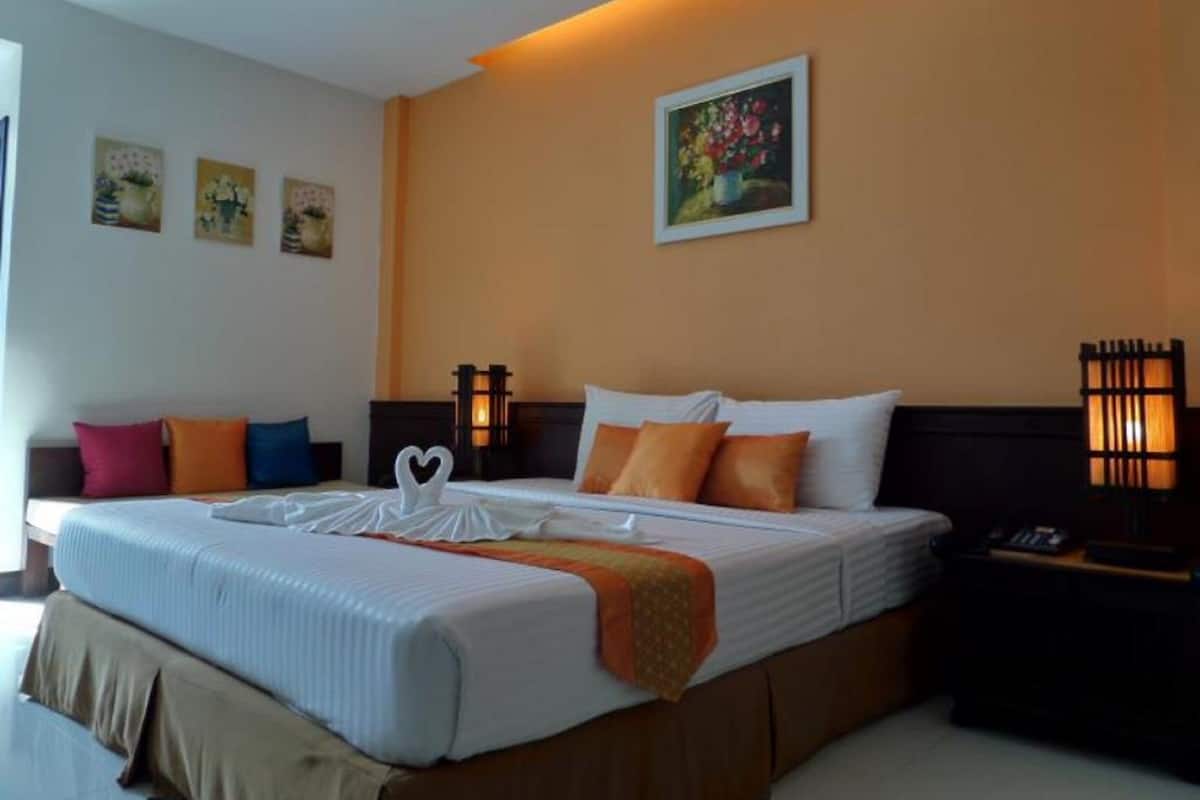 Une chambre d’hôtel avec un grand lit, plusieurs oreillers, une table de chevet avec une lampe et un mur orné de tableaux.