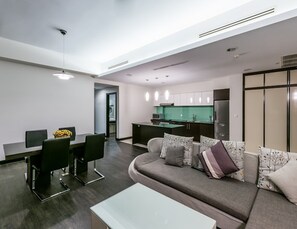 A modern living room with a sofa, a dining table, and chairs. There is a kitchen area with cabinets and a refrigerator. - Syphon Hotel & Apartment (Phnom Penh)