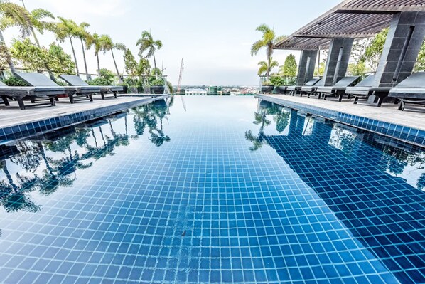 A clear blue infinity pool with lounge chairs and palm trees, surrounded by a covered area with columns.