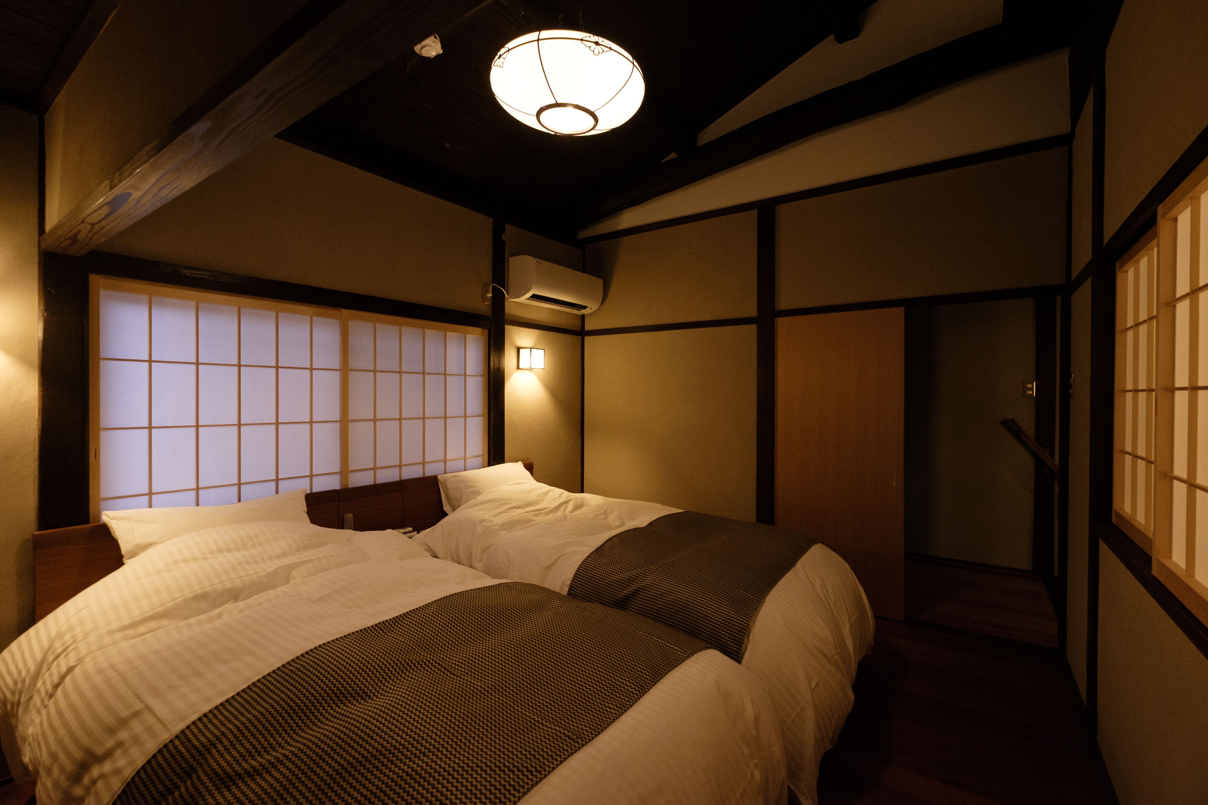 A traditional Japanese-style bedroom with tatami flooring, a low wooden bed frame, and a shoji screen behind the bed.