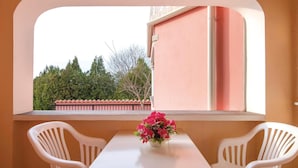 En balkon med et bord og to stole, en lyserød væg og udsigt til træer og en bygning.