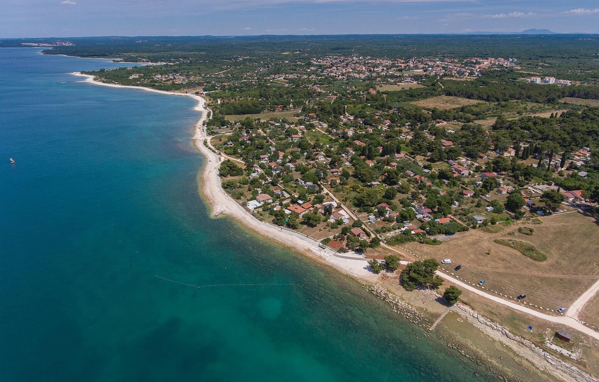 Vista aèria d'una població costanera amb platja, zones residencials i una combinació de vegetació i edificis.