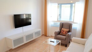 A living room with a flat-screen TV mounted on the wall, a glass coffee table, a sofa, and a chair with a patterned cushion. - Apartamento Sarah 2A, 2min to the beach and promenade, central and quiet. Free WIFI (Morro Jable)