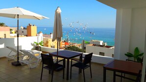 A balcony with a table and chairs, a white umbrella, and a view of the sea with birds flying. - Apartamento Sarah 2A, 2min to the beach and promenade, central and quiet. Free WIFI (Morro Jable)