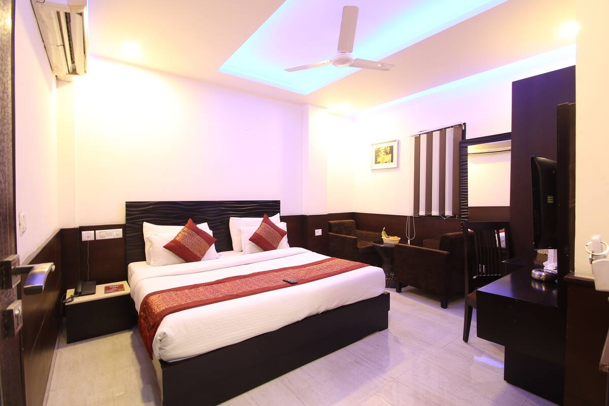 A hotel room with a large bed, a desk, a chair, a TV, and a ceiling fan.