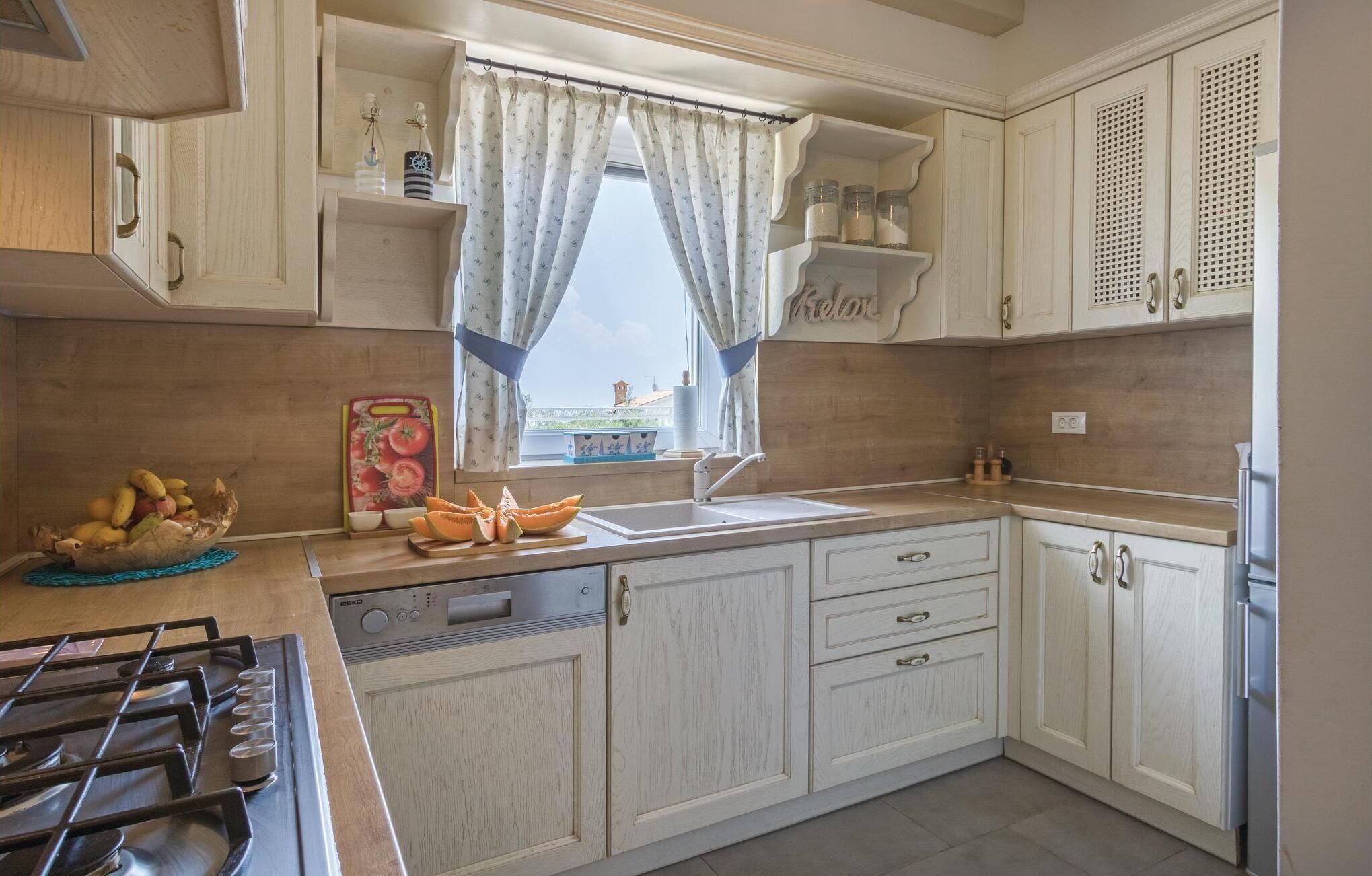 A kitchen with wooden cabinets, a gas stove, a sink, and a window with curtains.