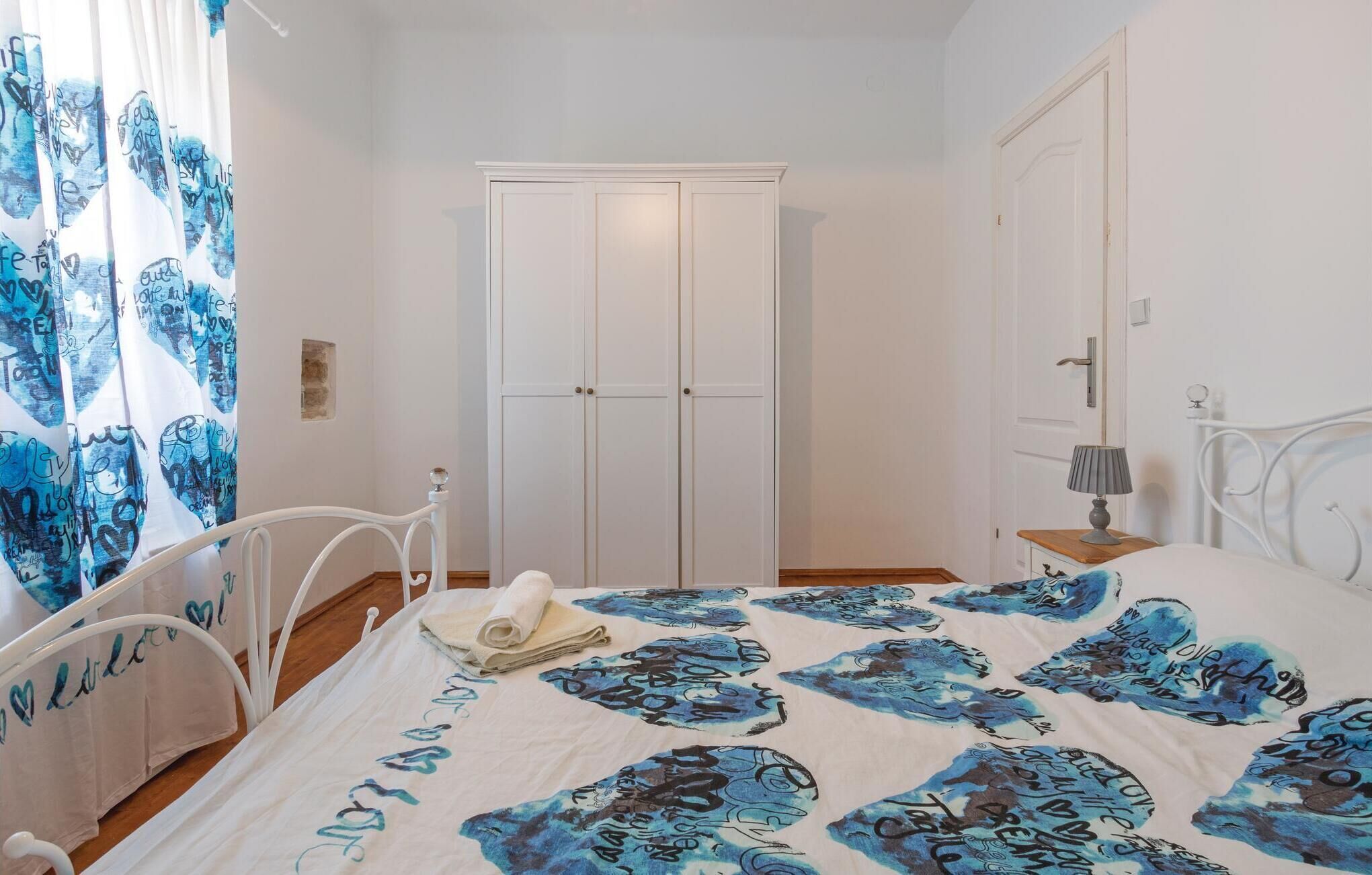 A bedroom with a bed, a bedside table with a lamp, a wardrobe, and a curtain with a blue pattern.