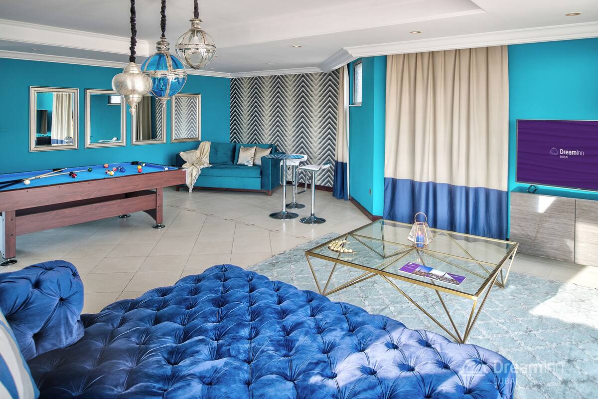 Una sala de estar moderna con una mesa de billar, un sofá azul y una mesa de centro de vidrio.