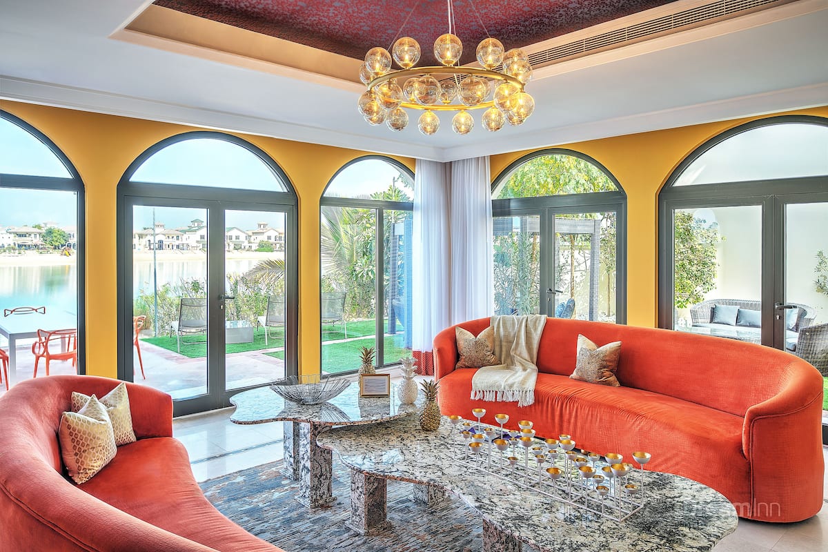Una sala de estar moderna con un sofá rojo, una mesa de centro de mármol y grandes ventanales con vistas al exterior.