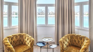A room with two plush armchairs, a small round table, and a view of a body of water and buildings through large windows. - Dream Inn Dubai-Palm Island Retreat Villa (Dubai)