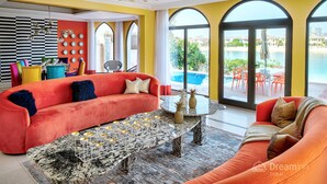 A vibrant living room with a red sofa, a marble coffee table, and a view of a pool through large arched windows. - Dream Inn Dubai-Palm Island Retreat Villa (Dubai)