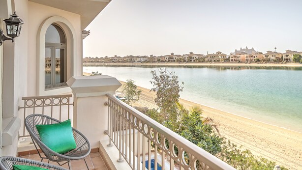 A balcony with wicker chairs and cushions, overlooking a beach and a body of water with buildings in the background. - Dream Inn Dubai-Palm Island Retreat Villa (Dubai)