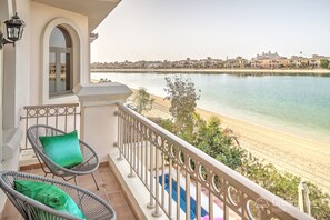 A balcony with wicker chairs and cushions, overlooking a beach and a body of water with buildings in the background. - Dream Inn Dubai-Palm Island Retreat Villa (Dubai)