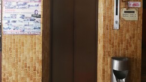 Ein Aufzug mit brauner Tür, einem Mülleimer und einem an der Wand montierten Telefon.