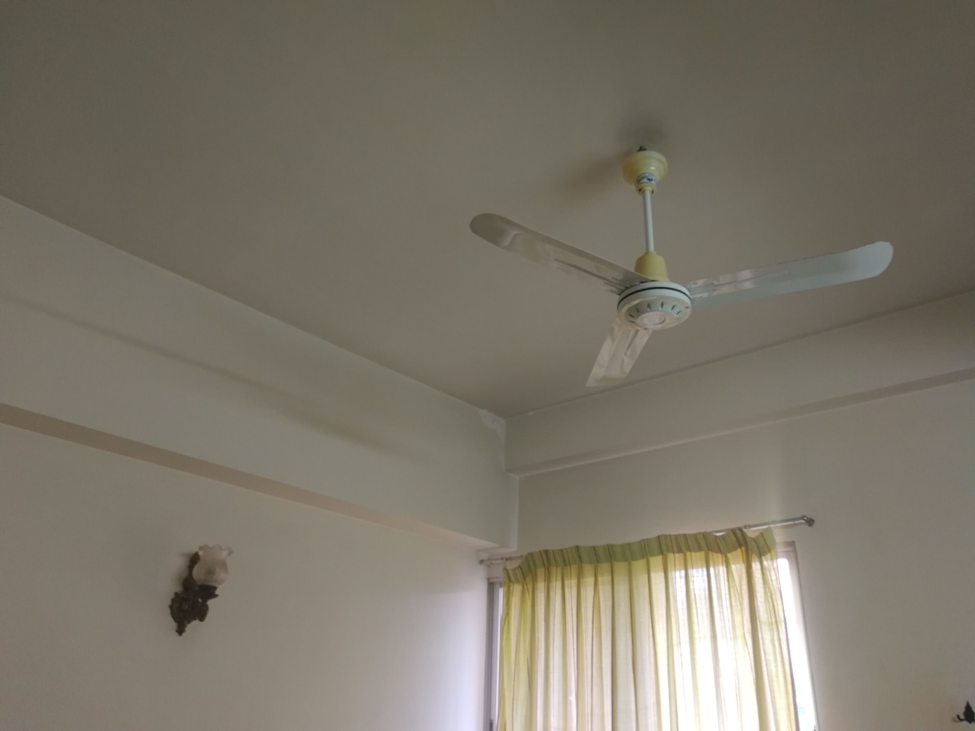 A room with a ceiling fan, a window with curtains, and a wall-mounted light fixture.