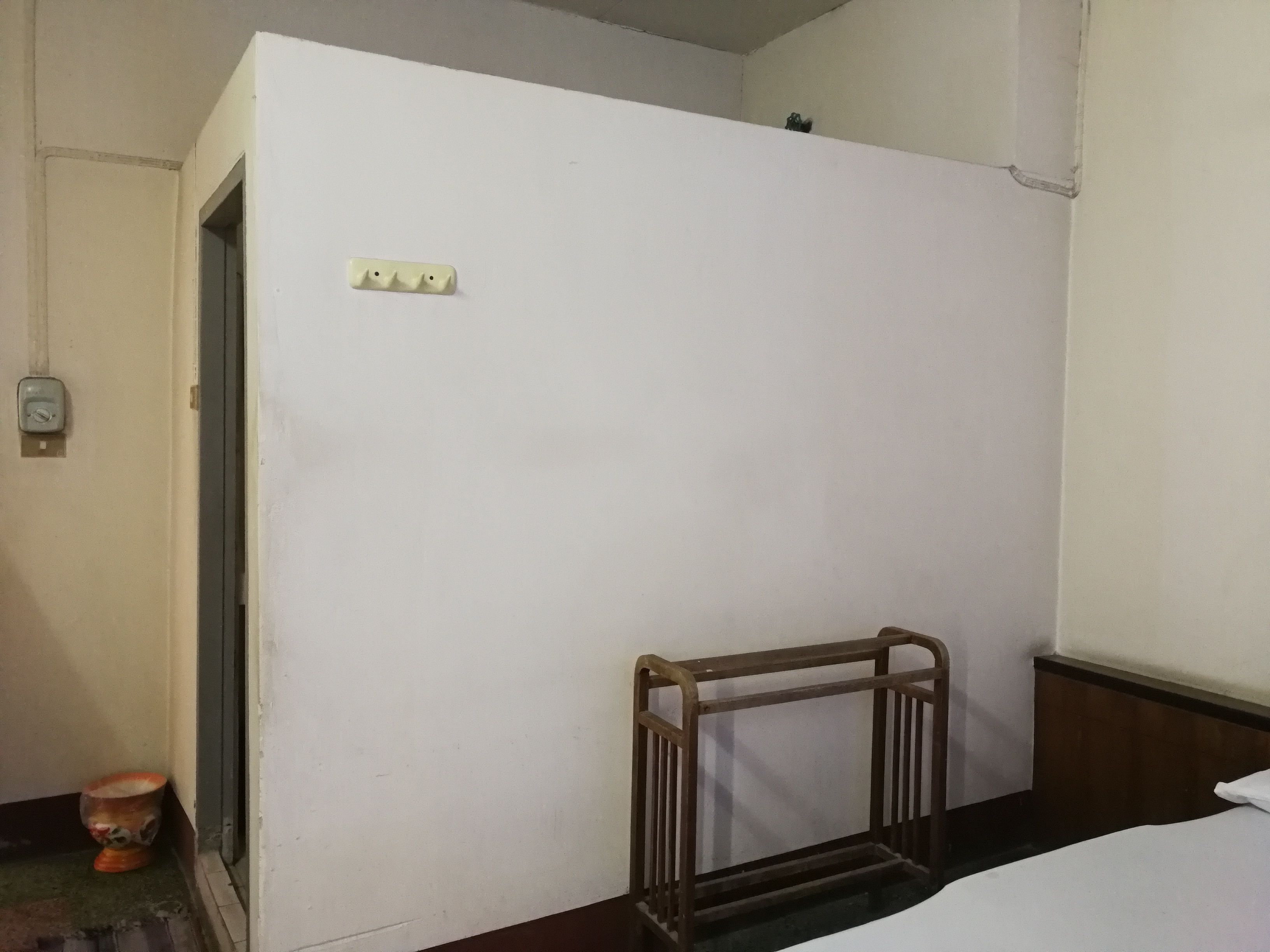 A small, sparsely furnished room with a single bed, a wooden chair, and a door leading to another room.
