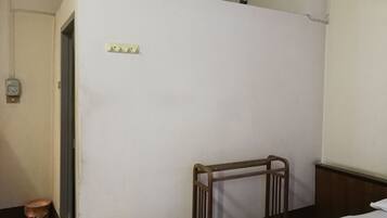 A small, sparsely furnished room with a single bed, a wooden chair, and a door leading to another room.