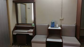 A compact bathroom with a vanity, mirror, and a small seating area.