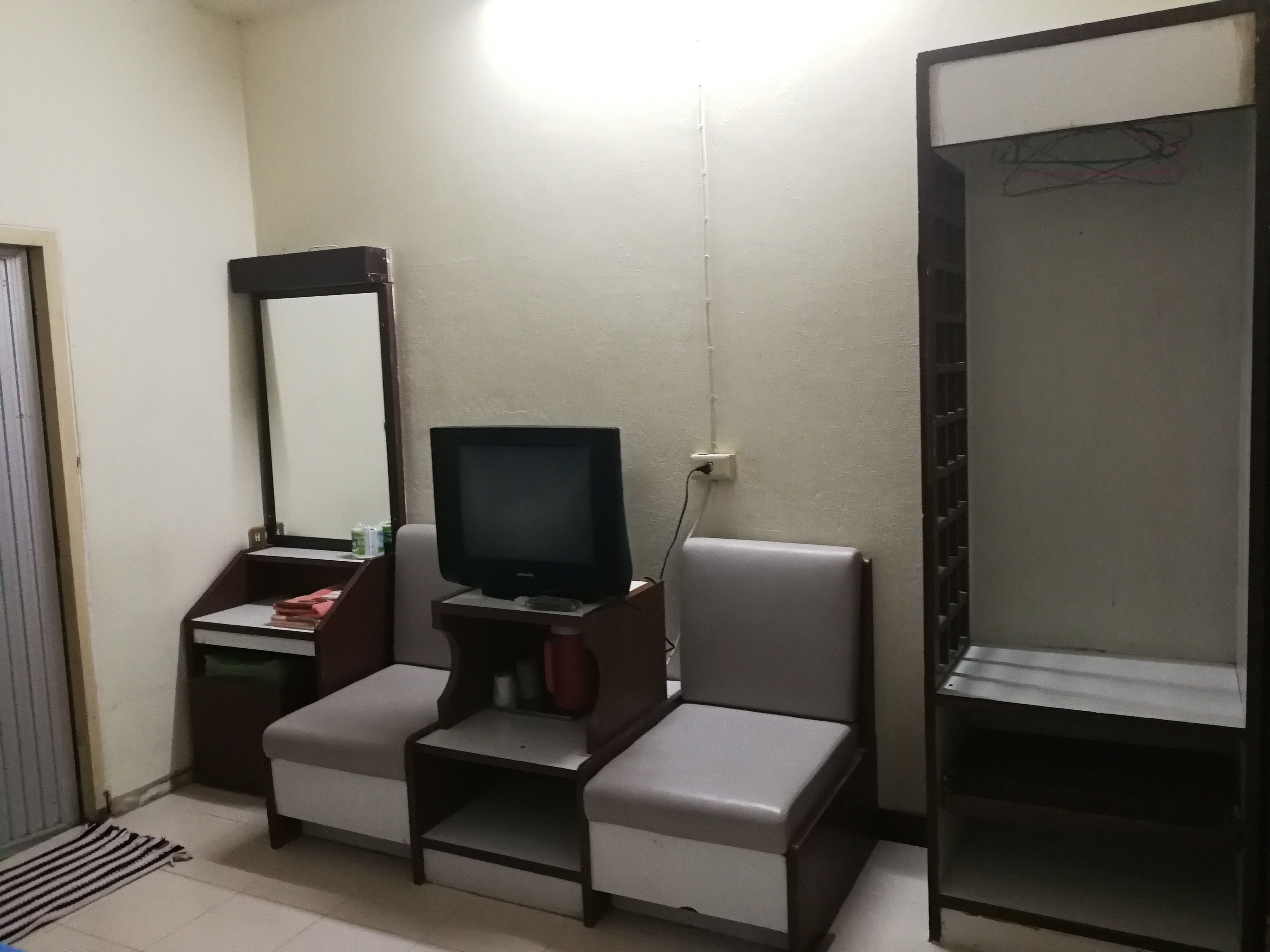 Una habitación pequeña con televisión sobre un mueble bajo, un espejo, una mesita y una silla.